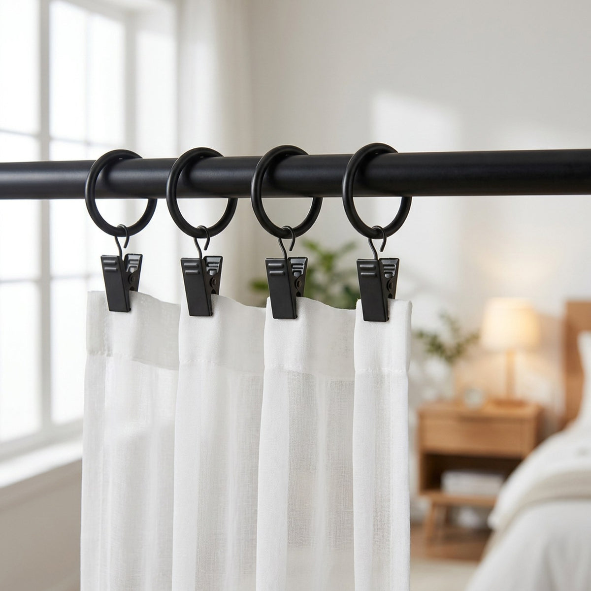 Anneaux à rideau à clips noirs sur tringle avec voilage blanc dans une chambre lumineuse