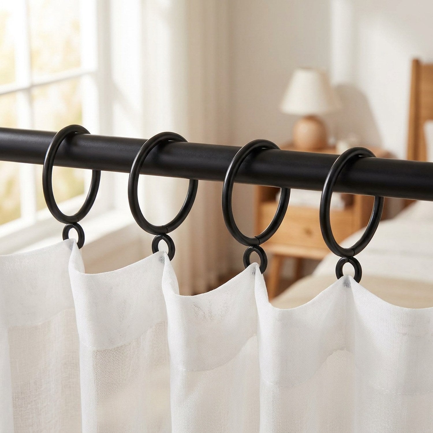 Anneaux à rideau noirs sur tringle avec voilage blanc dans une chambre lumineuse