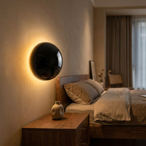 Applique murale noire brillante allumée au dessus d'une table de chevet en bois dans une chambre cosy