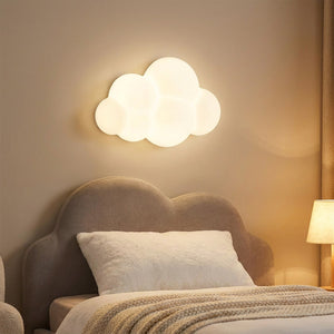 Applique murale nuage allumée au dessus d'une tête de lit rembourrée avec coussin moelleux