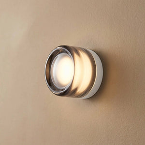 Applique murale ronde en verre gris fumé diffusant une lumière chaude sur un mur clair