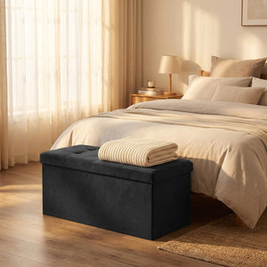 Couverture tricotée pliée sur un banc coffre en velours noir au pied d'un lit