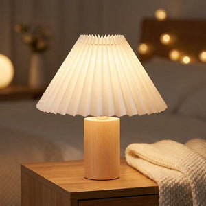 Abat-jour plissé blanc en tissu sur pied en bois clair éclairé sur une table de chevet