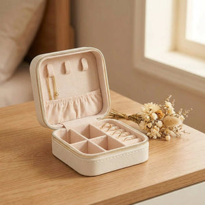 Boîte à bijoux de voyage en cuir crème à fermeture zippée ouverte sur intérieur velours avec bagues sur une table de chevet