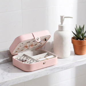 Boite à bijoux rose ouverte sur une étagère de salle de bain en marbre avec distributeur de savon et succulente