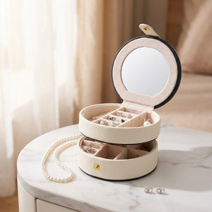 Boîte à bijoux ronde blanche ouverte sur un plan en marbre avec collier de perles et boucles d'oreilles