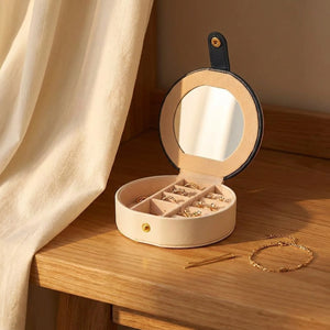 Boîte à bijoux ronde blanche ouverte sur une table en bois avec bagues et boucles d'oreilles
