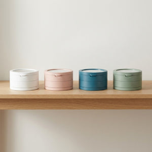 4 boîtes à bijoux rotatives en rangée sur étagère en bois dans les coloris blanche, rose, bleu et verte