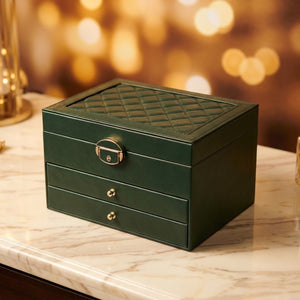Boîte à bijoux multicouche en cuir vert foncé avec motif matelassé et fermoir doré sur marbre