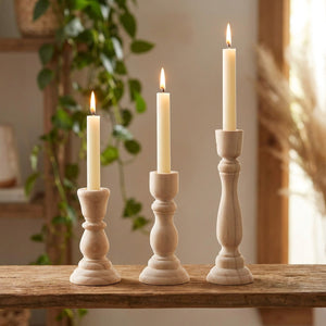 Bougeoirs en bois brut allumés sur une étagère bohème avec plante verte