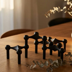 Trois bougeoirs moléculaires noirs séparés posés côte à côte sur une table en bois