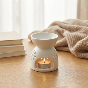 Brûle-parfum en céramique allumé sur un bureau près d'une fenêtre avec plaid