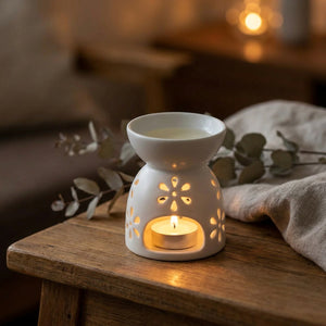Brûle-parfum en céramique blanche ajourée à motifs floraux posé sur une table en bois avec bougie allumée