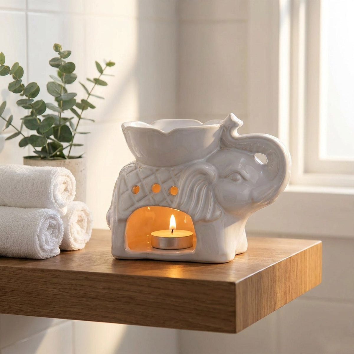 Brûle-parfum éléphant allumé posé sur une étagère de salle de bain avec serviettes roulées et plante verte
