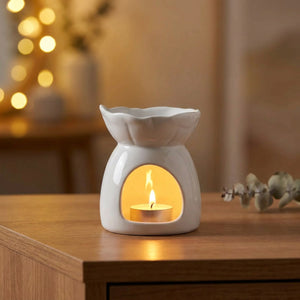 Brûle-parfum céramique blanc en forme de fleur avec bougie chauffe-plat allumée sur une table en bois
