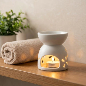 Brûle-parfum en céramique allumé sur une étagère de salle de bain avec serviette et plante