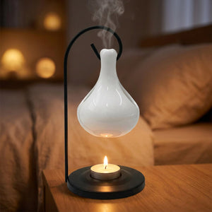 Brûle-parfum en céramique blanche allumé sur une table de chevet le soir