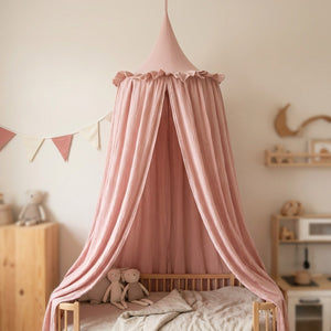 Ciel de lit rose en mousseline de coton au-dessus d'un lit bebe dans une chambre douce