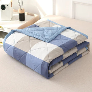 Couette d'été à carreaux bleus et gris pliée montrant le matelassage en losanges