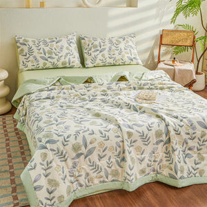 Couette d'été vert sauge posée sur un lit avec taies assorties et coussins