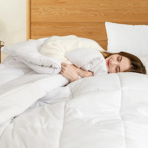 Femme blottie sous une couette blanche moelleuse dans un lit douillet