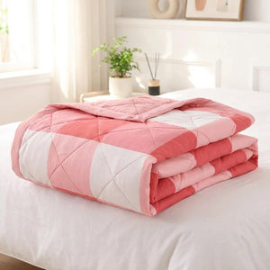 Couette d'été matelassée à carreaux roses et corail pliée sur un lit
