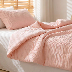 Couette d'été rose en coton seersucker posée pliée sur un lit dans une chambre lumineuse