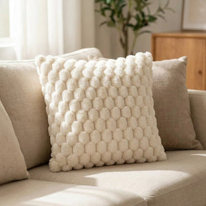 Housse de coussin à pompons en relief de couleur crème posée sur un canapé clair lumineux