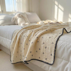 Couverture d'été enfant en gaze de coton à motifs petites cerises drapée sur un lit