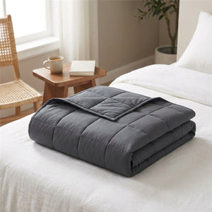 Couverture lestée grise pliée au pied d'un lit avec une chaise en rotin