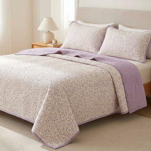 Couvre-lit matelassé imprimé floral violet posé sur un lit dans une chambre lumineuse