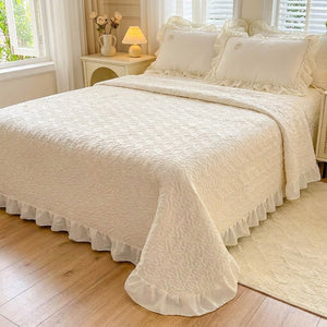 Couvre-lit matelassé beige à motif de cœurs et volant froncé installé sur un lit dans une chambre lumineuse