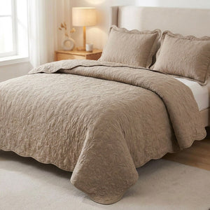 Couvre-lit matelassé taupe au motif baroque en relief installé sur un lit dans une chambre chaleureuse avec deux taies assorties
