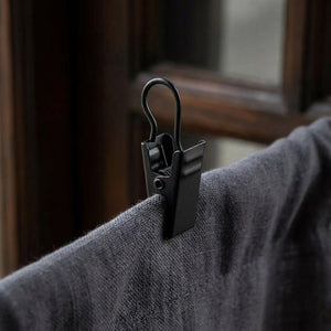 Détail macro d'un crochet à clip noir mat fixé sur un rideau en lin gris