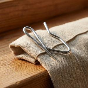 Détail macro d'un crochet de rideau en métal pincé dans un pli de tissu
