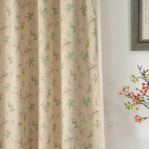 Rideau boho en lin motif feuillage vert à pompons devant une fenêtre