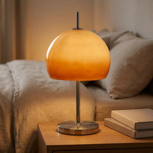 Lampe à poser champignon orange allumée sur une table de chevet à côté d'un lit