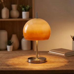 Lampe à poser champignon orange allumée sur un bureau en bois le soir