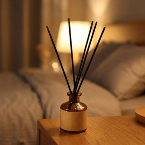 Diffuseur de parfum à bâtonnets sur une table de chevet près d'une lampe chaleureuse