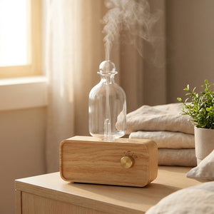 Diffuseur d'huile essentielle en verre posé sur une table de chevet en bois avec une fine brume parfumée qui s'élève