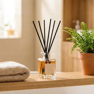 Diffuseur de parfum à bâtonnets sur une étagère de salle de bain près d'une serviette et d'une plante verte