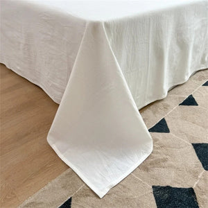 Coin du drap plat en coton drapé sur le matelas avec tissu qui retombe au sol
