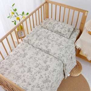 Parure de lit bébé motif nature au trait installée sur un lit à barreaux