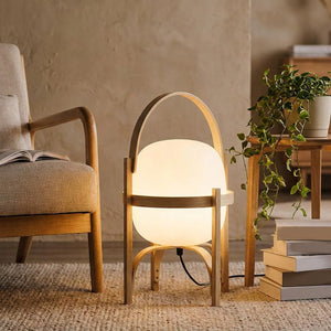 Lampe lanterne en bois posee pres d un fauteuil de lecture avec une plante verte