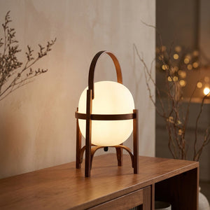 Lampe lanterne en bois teinte noyer avec globe de verre opale allumee sur une console