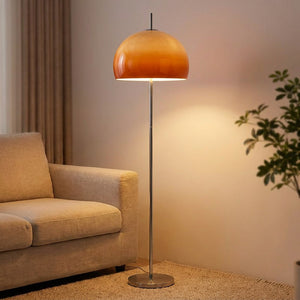 Lampadaire champignon en verre orange dégradé allumé près d'un canapé dans un salon chaleureux