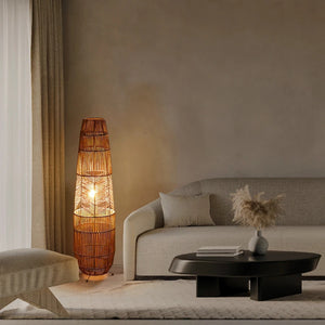 Lampadaire en rotin allumé dans un salon avec canapé beige et table basse