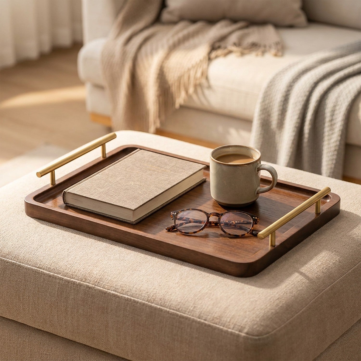 Plateau en bois à poignées dorées posé sur un pouf avec un livre une tasse de café et des lunettes