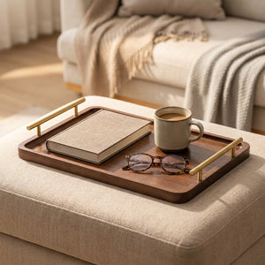 Plateau en bois à poignées dorées posé sur un pouf avec un livre une tasse de café et des lunettes