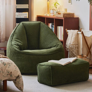 Fauteuil pouf et repose-pieds vert foncé dans un salon bohème avec plaid en crochet